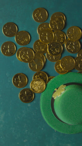 Vertical-Video-Overhead-Studio-Shot-Of-Green-Leprechaun-Top-Hat-And-Piles-Of-Gold-Coins-To-Celebrate-St-Patricks-Day